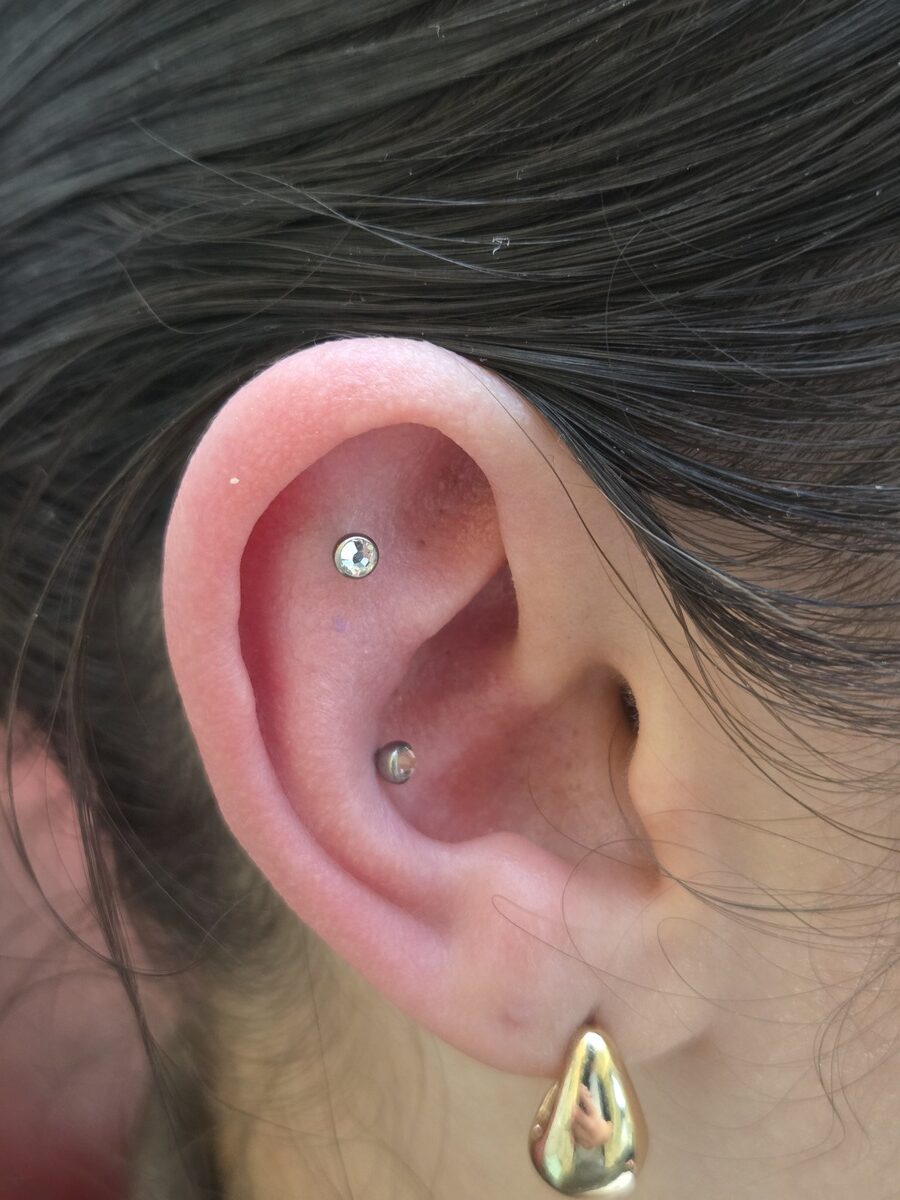 Nahaufnahme eines Ohrs mit zwei silbernen Piercings und goldener Creole