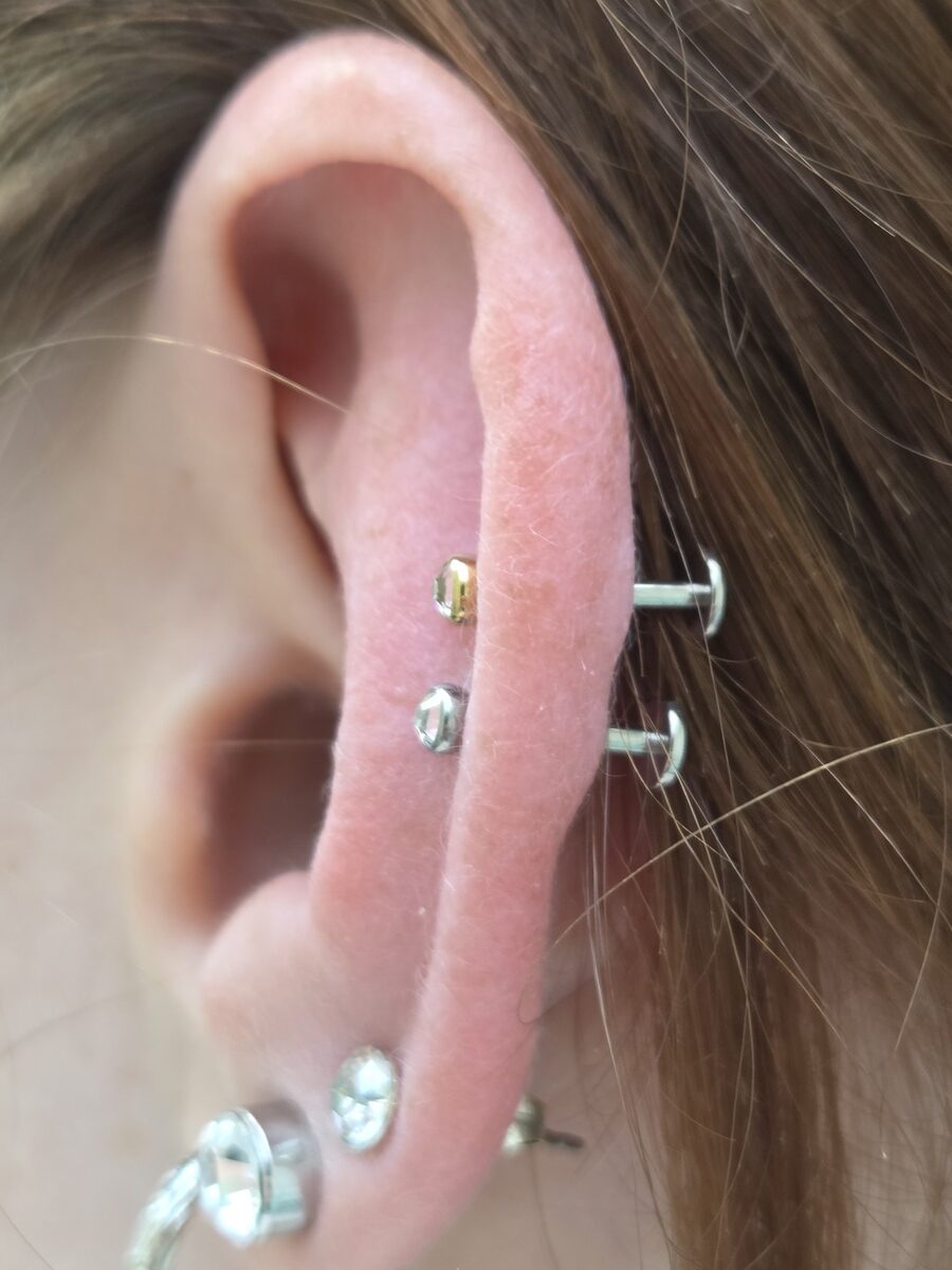 Nahaufnahme eines Ohrs mit neutralem Ausdruck, rosa und mit Piercings