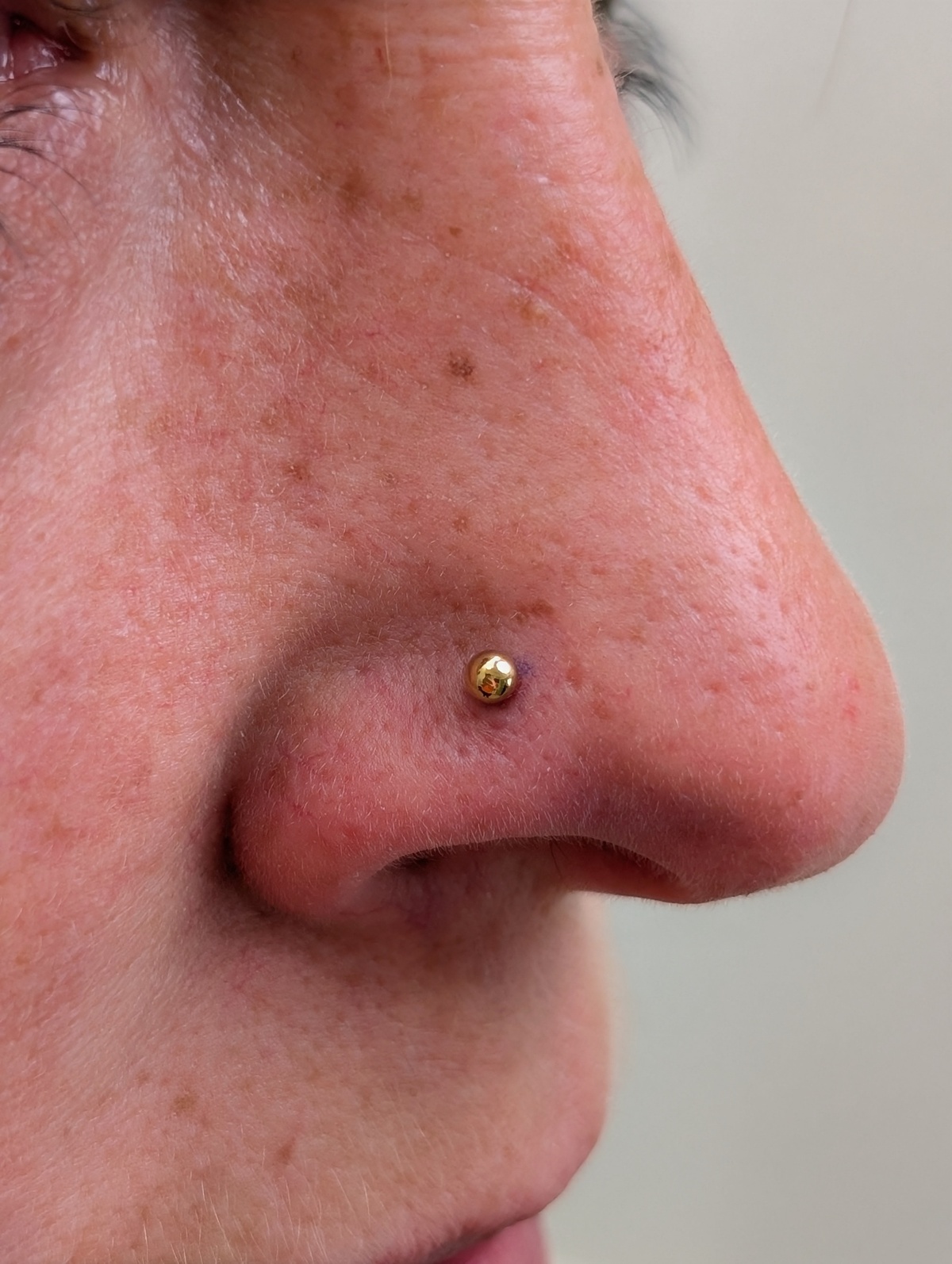 Nahaufnahme eines ernsten Gesichts mit rotem Nasenpiercing in Gold