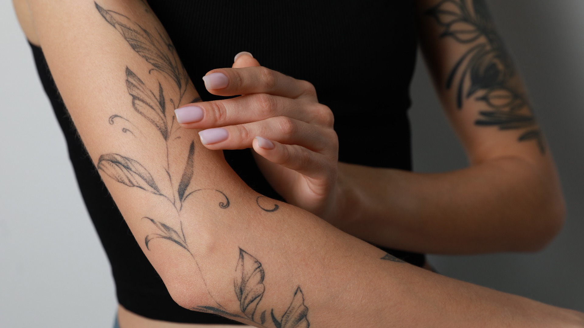 Frau, die sich vor einem hellen Hintergrund Creme auf ihren mit Tattoos verzierten Arm aufträgt